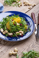 Vegan plant based salad with fresh  arugula, orange, pomegranate seeds, cashews