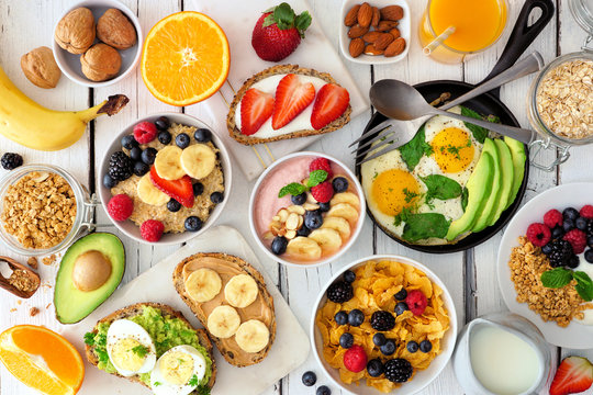 Healthy breakfast table scene with fruit, yogurts, oatmeal, smoothie bowl, cereal, nutritious toasts and egg skillet. Top view over a white wood background.