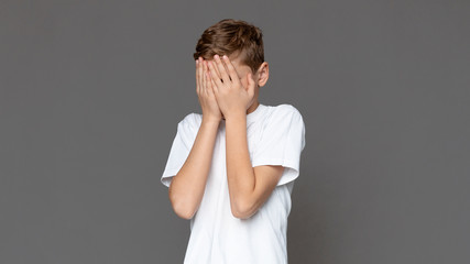 Teen boy hiding face in hands, grey background