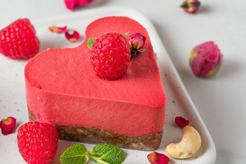 raw vegan raspberry heart shaped cake or cheesecake with fresh berries, nuts, mint and dried flowers. Valentines day dessert