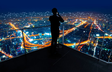 Businessman standing using smart phone in modern space watching city night view.Business Wireless...