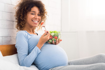 Healthy snack. Afro expectant girl enjoying fresh vegetable salad