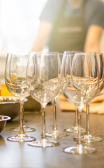 Wine glasses standing side by side on a table with candle in the sun light, blurred background.