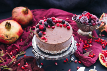 Delicious raw vegan cake on a silver plate with frozen raw berries on top surrounded by autumn red fruits and a red rag