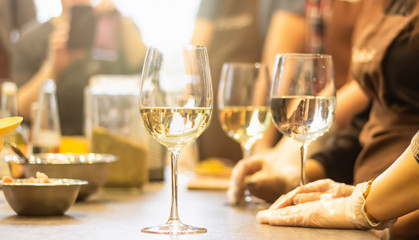 Refreshing white wine in glasses standing side by side on a table with candle in the sun light, blurred background.
