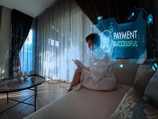 Woman in white bathrobe siting on the armchair near the window in hotel room using smartphone for online payment and banking and online shopping.