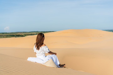 Fototapeta na wymiar Young beautiful Asian woman posing in a white dress in white sand dune desert, Muine Vietnam.