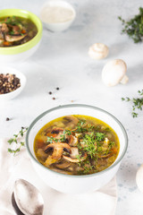 Homemade thick vegetarian mushroom soup with barley and vegetables with herbs in a ceramic bowl on a light grey stone background. Delicious cozy first course, comfort food.