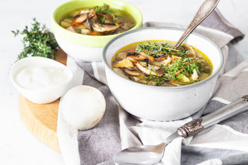 Homemade thick vegetarian mushroom soup with barley and vegetables with herbs in a ceramic bowl on a light grey stone background. Delicious cozy first course, comfort food.