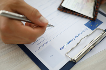 Close-up of persons hand holding silver pen and filling application for schengen visa. Essential step to entry in european union. Eu and travelling abroad concept