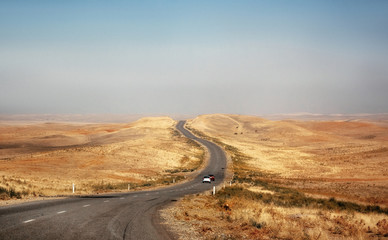 Cars ride on desert road through steppe in Kazakhstan