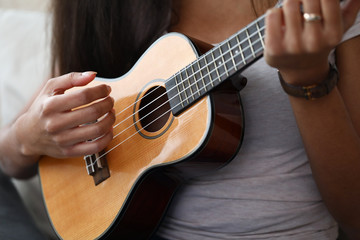 Close-up of latino female hands playing on brown ukulele. African-american woman learning new melody at home. Music talent, art and entertainment concept