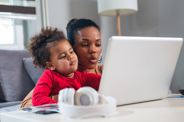 African American mother with little daughter using laptop together.
