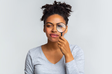 Suspicious young woman looking at camera through magnifier