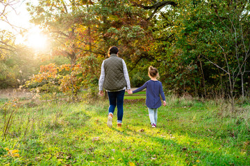 Mother and daughter holding hands while walking in a park outdoors