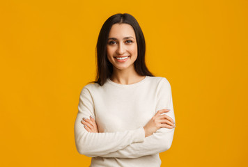 Beautiful brunette woman standing with folded arms over yellow background - Powered by Adobe