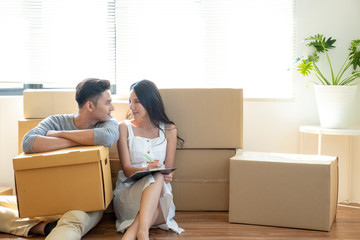 Happy young Asian couple having break and looking each other and smiling during moving to new house