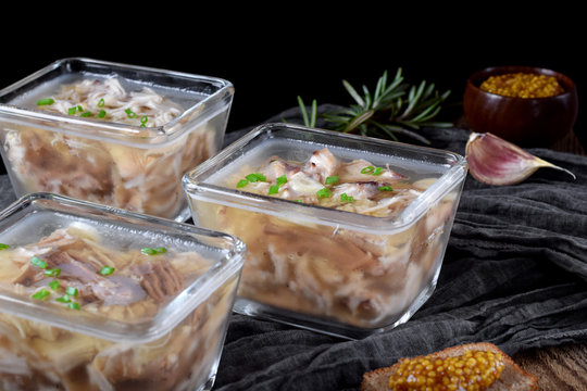 Holodets with chicken and pork meat in glass portion bowls against the dark background