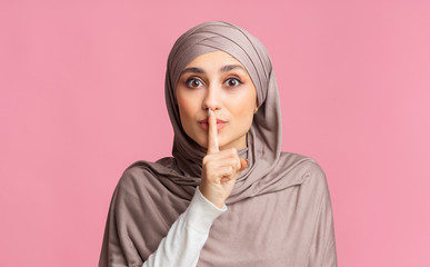 Secret. Muslim woman showing hush sign, putting finger on lips