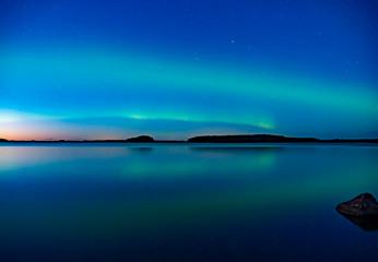 Fototapeta na wymiar Northern lights dancing over calm lake. Farnebofjarden national park in Sweden.