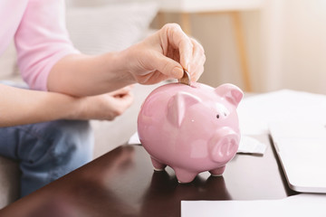 Obraz na płótnie Canvas Senior lady putting coins into pink piggy bank