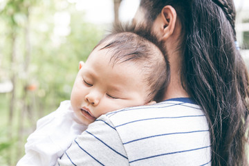Obraz premium An Asian boy is sleeping deeply On the mother's shoulder with blur background, to family concept.