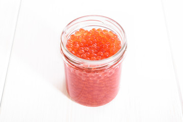 Red caviar in glass jar on white wooden background