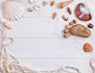 Seashells, rocks in the shape of foot and white sand and rope on a white wooden background. Nautical background. Text space. Top view.