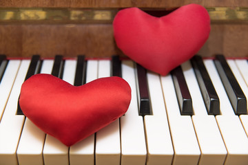 Two red hearts lie on the piano keyboard. The concept of music for love.