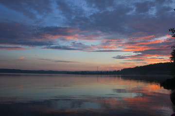 Dramatic purple blue sunset with reflection of sky and clouds over a calm lake during twilight. Photography of evening mountain lake