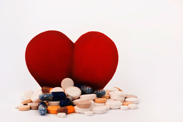 Heap of colorful pills, tablets, capsules and a figure of a cardboard red heart on white...