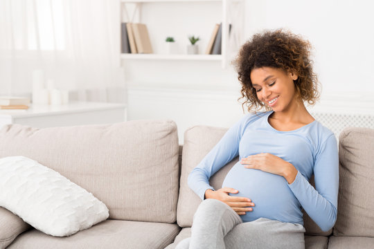 Enjoying pregnancy. Afro girl touching belly and smiling