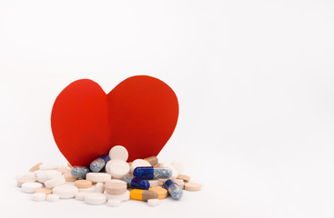 Heap of colorful pills, tablets, capsules and a figure of a cardboard red heart on white...