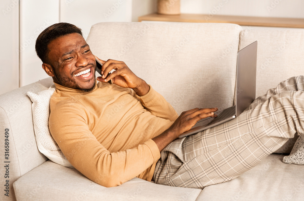 Poster man talking on phone working on laptop lying on sofa