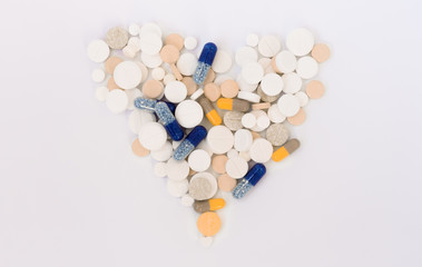 Heap of colorful pills in the shape of a heart, tablets and capsules on white background. Drug...