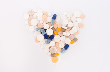 Heap of colorful pills in the shape of a heart, tablets and capsules on white background. Drug prescription for treatment medication health care concept, top view with copy space.