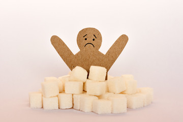 figure of a cardboard man surrounded by refined sugar cubes on white background, diabetes protection medical concept.
