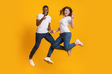 Playful multiracial couple jumping in air, having fun together