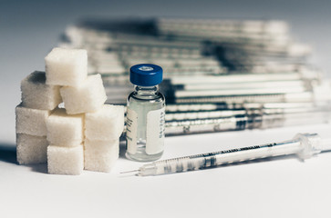 bottle of insulin for diabetes and injection syringe, healthcare concept with refined loaf sugar cubes pile of syringes on background.