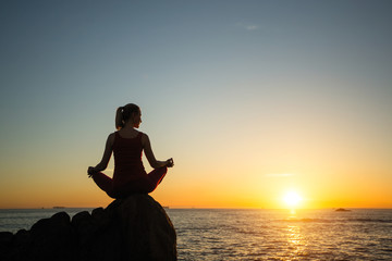 Yoga woman on the ocean coast during warm sunset.