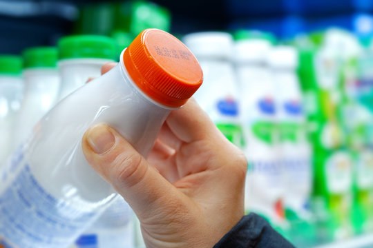 Buyer checks expiration date of dairy product before buying it. Womans hand holding milk bottle in supermarket. Close-up.
