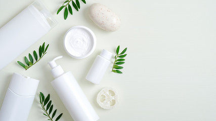 Obraz na płótnie Canvas Organic herbal cosmetic products on green background. Top view beauty spa cosmetic bottle packaging, hand cream, lotion, bath sponge, natural soap and green leaves. Minimalist beauty product mockups