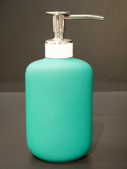 turquoise plastic cosmetic bottle with a silver metal cap and a pump on a dark background, close up, soap container, face cream, hair shampoo, body bath gel, empty packaging