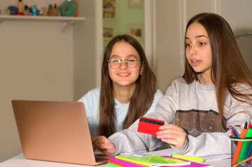 Two teen girls surf the Internet on their laptop, look for products of interest to them and make purchases with a credit card. Teenagers' concept of navigation, research and shopping