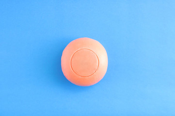 Round natural soap of coral color on a blue background.