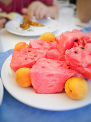 Slices of fresh ripe watermelon and apricots on a round white plate on the table close-up.