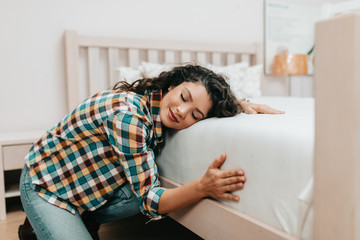 Beautiful and happy middle age woman choosing new bed and mattress in big furniture store