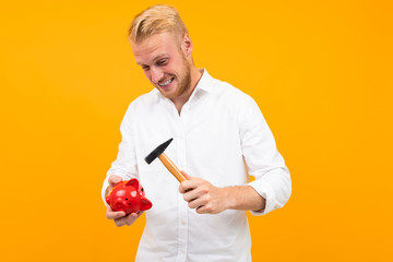 handsome man in a white shirt smashes a piggy bank with a hammer on a yellow background