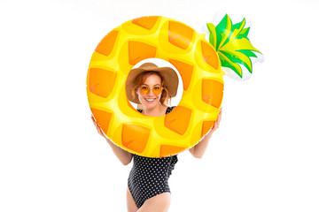 beautiful girl dressed in retro swimsuit and a straw hat holds a swimming circle in the shape of pineapple on a white background