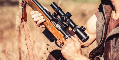 Male hunter in ready to hunt. The man is on the hunt, sport. Hunter man. Hunting period. Male with a gun, rifle. Man is charging a hunting rifle. Process of hunting during hunting season